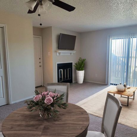 Living Oaks Apartments living room rendering with a dining table and chairs, ceiling fan, coffee table and rug, TV, fireplace, and sliding doors out to a private patio