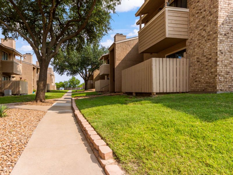 Living Oaks Apartments building exterior with a walk path, green grass, and mature trees